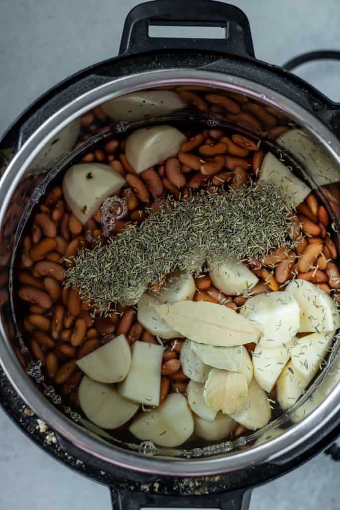 Instant pot filled with soaked beans, potatoes, bay leaves and thyme.