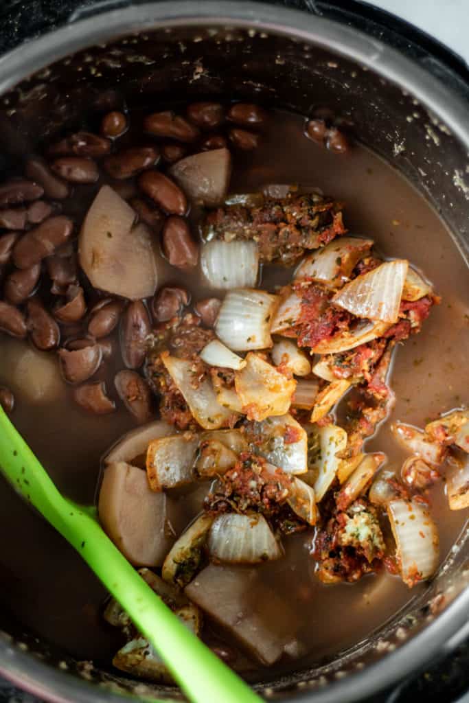 Adding the sautéed onions to the instant pot after beans have cooked.