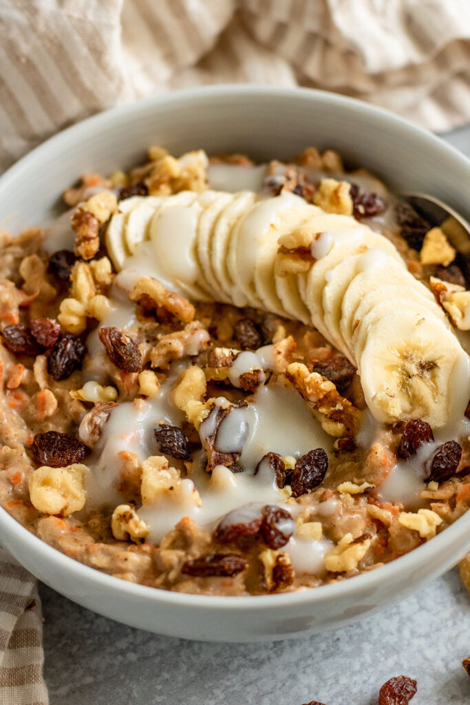 Side view of a bowl of oats cooked with shredded carrots, spices, raisins and walnuts.