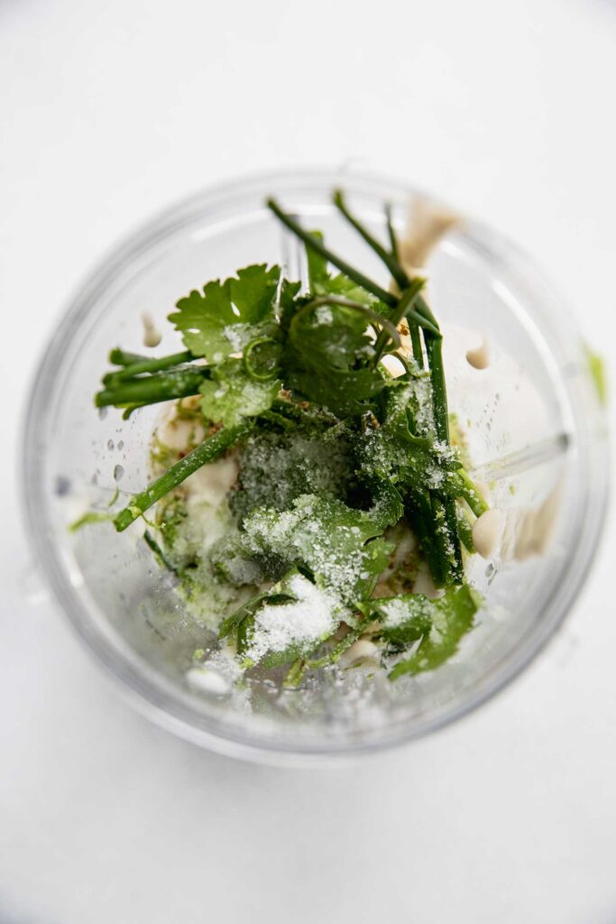 Blender cup full of herbs, yogurt, and avocado.