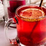 Close up of a mug of hibiscus tea after an ice cube has melted and a mug in the background with two large ice cubes stacked on top of each other.