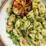 Lemon basil pasta served in a white bowl with seared lemon half on the side.