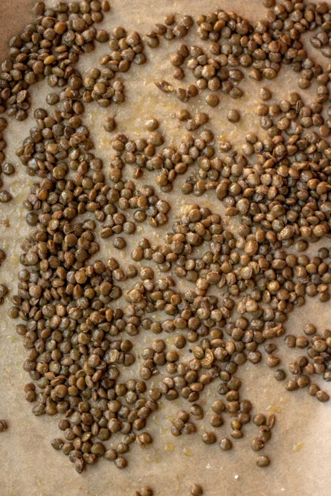 Lentils tossed with oil and salt on a baking tray.