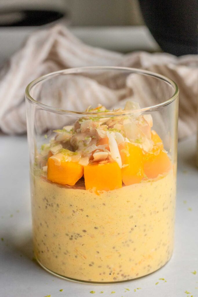 A single jar of mango flavored overnight oats topped with cubed mango, lime zest and coconut flakes.