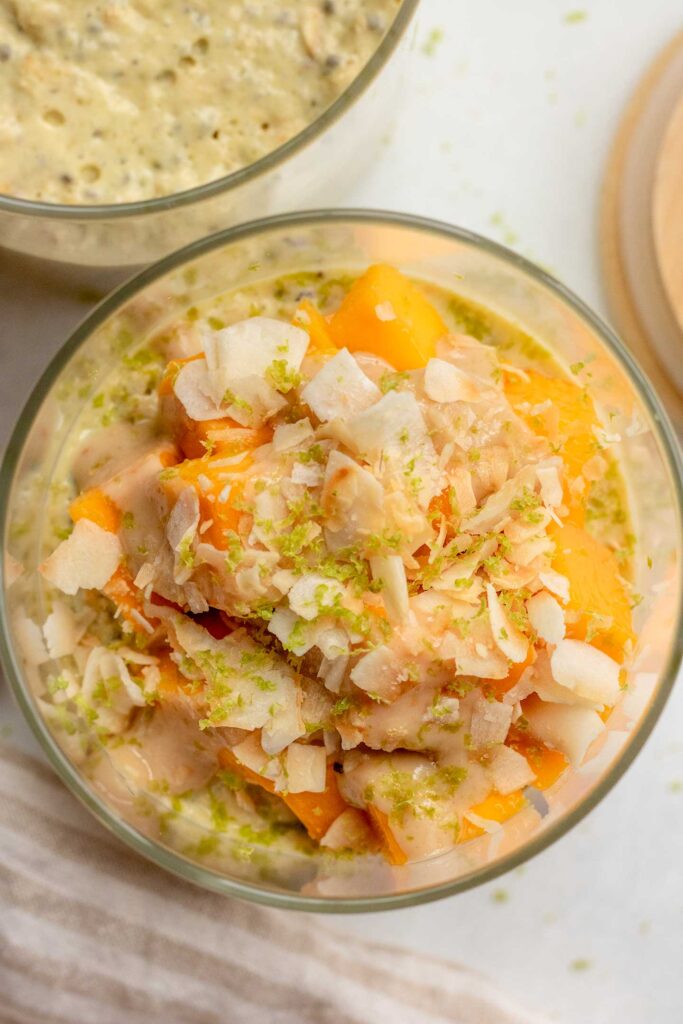 Top down view of a jar of mango flavored overnight oats showing the toppings including mango, lime zest and cashew butter.