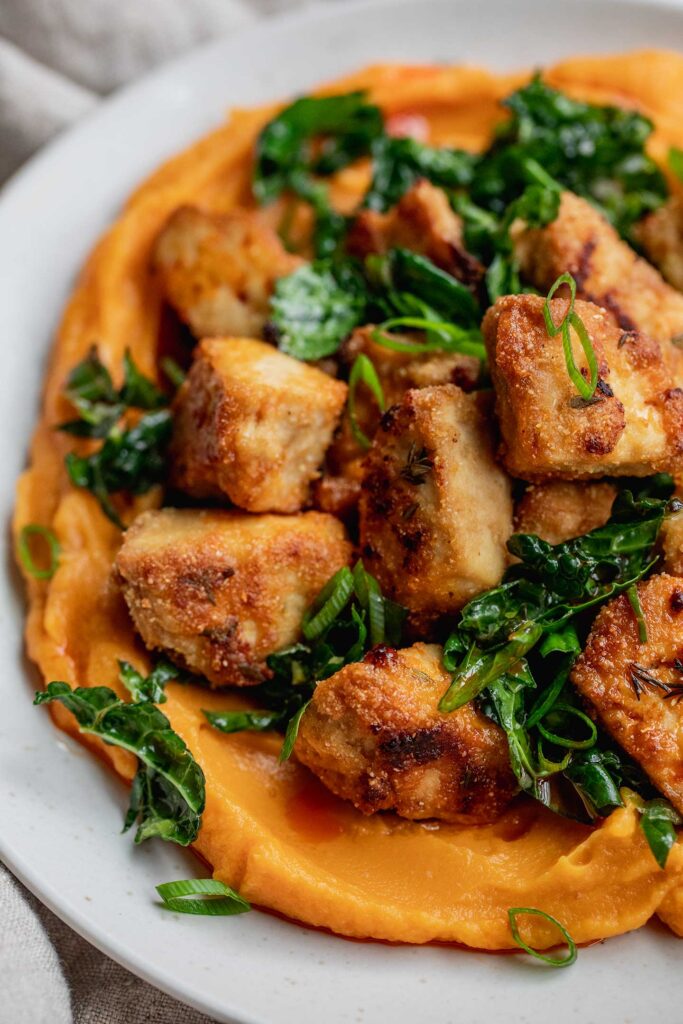 Close up look at blended sweet potato topped with marinated kale and crispy tofu.