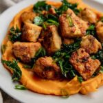 Plate of sweet potato puree topped with marinated kale and crispy tofu.