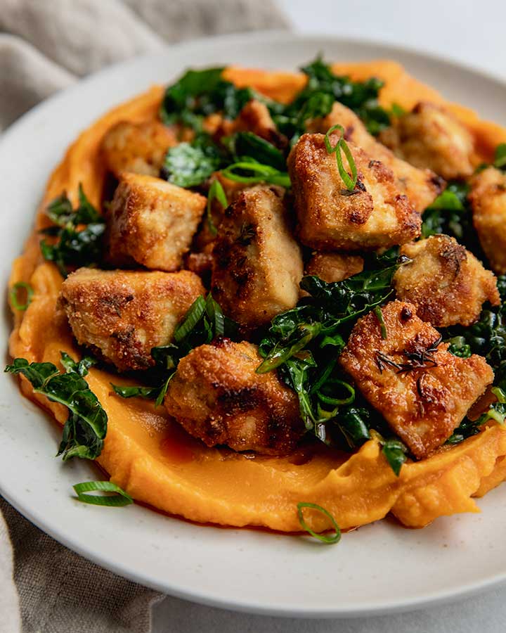 Plate of sweet potato puree topped with marinated kale and crispy tofu.