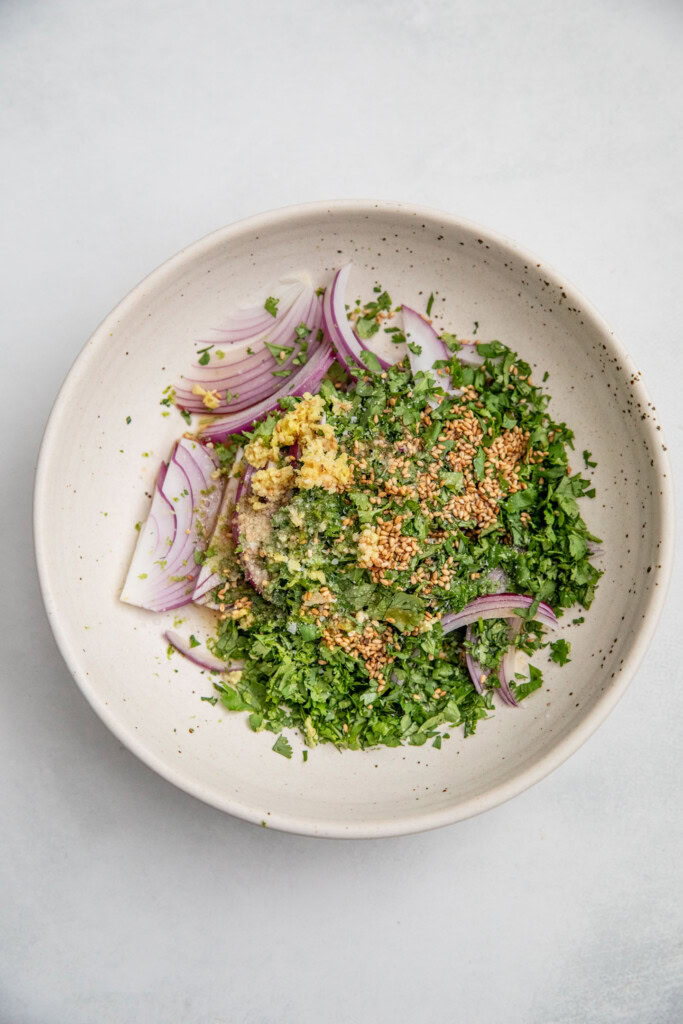 Bowl of red onions, herbs, ginger, lime, sesame seeds and sesame oil.