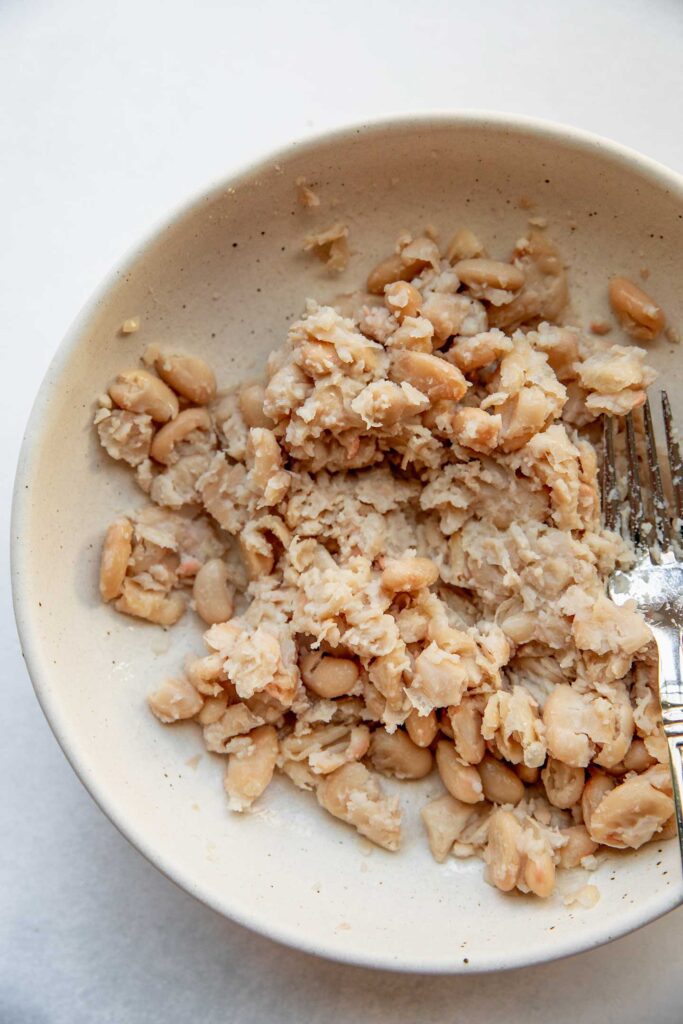 Mashing white beans in a bowl with a fork.
