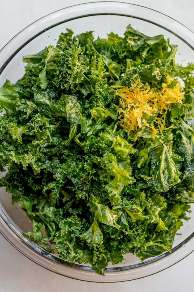 Large glass bowl filled with chopped kale, lemon zest, lemon juice and salt.