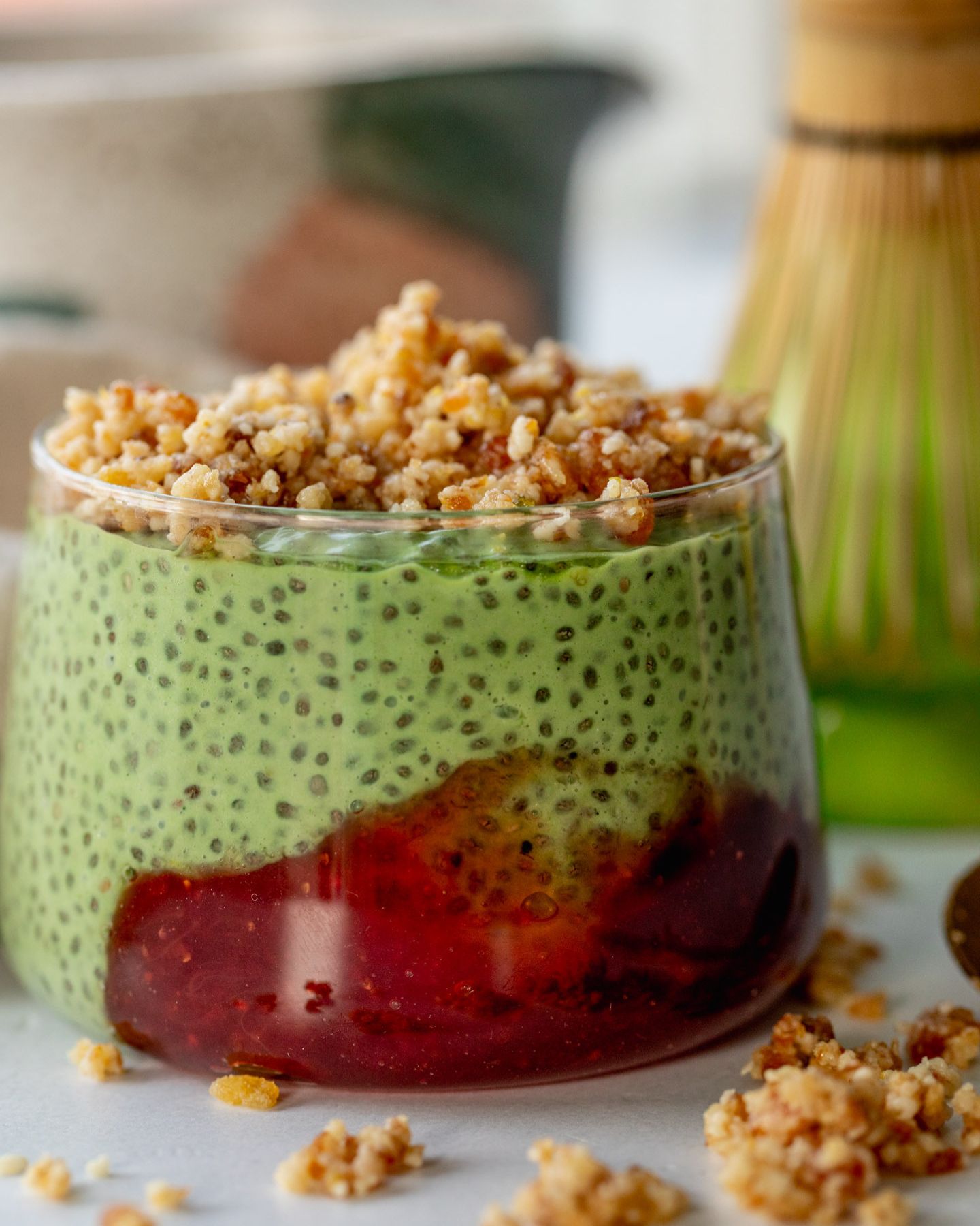 Close up of a jar of matcha pudding served with a dollop of strawberry jam and pie crust crumble on top.