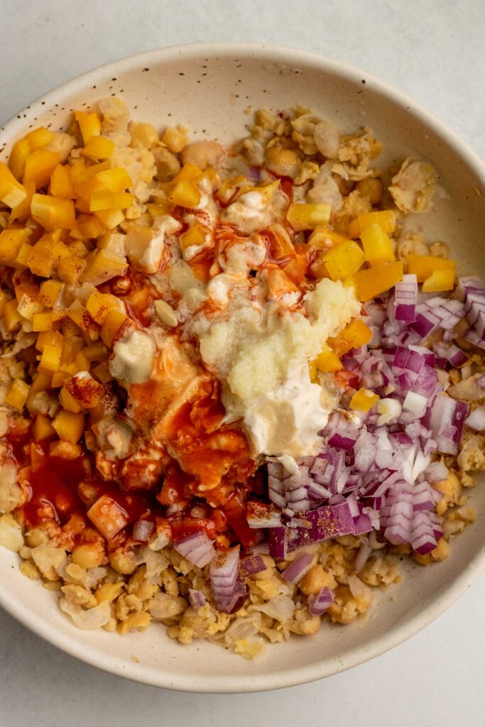 Mixing the chickpeas and topped with onion, bell pepper, seasonings, garlic, tahini, buffalo sauce and yogurt.