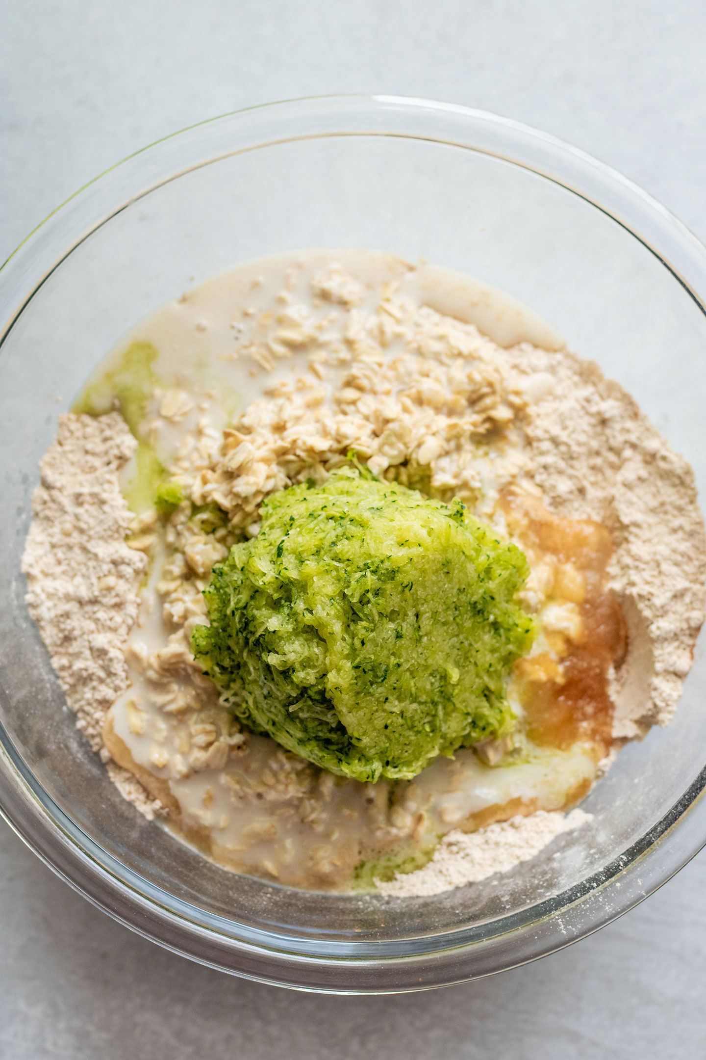 Adding the soaked oats and shredded zucchini to the bowl of dry ingredients.