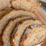 The loaf of whole wheat bread fully sliced and fanned out on a wooden cutting board.