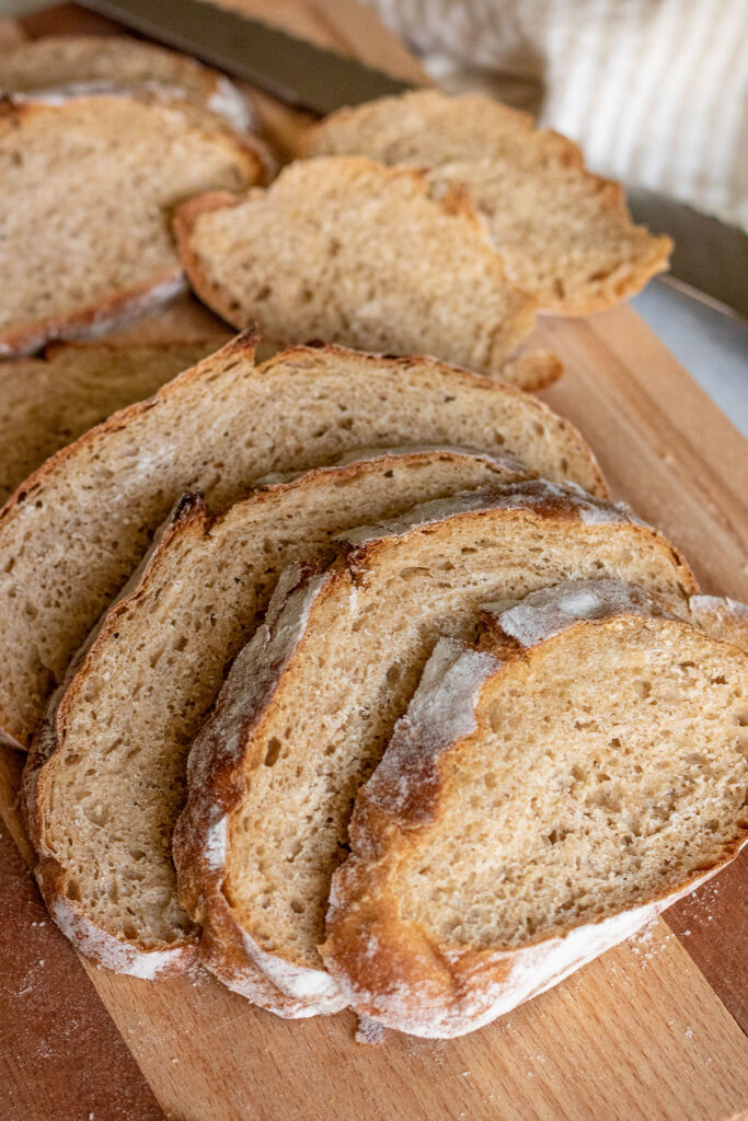 The loaf of whole wheat bread fully sliced and fanned out on a wooden cutting board.