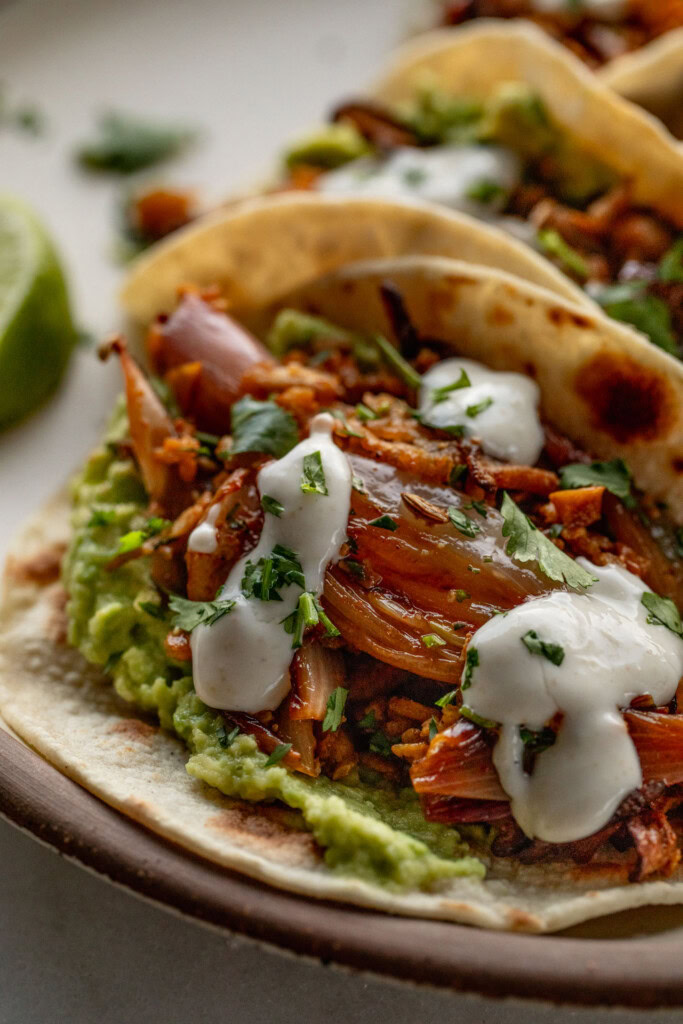 Close up of a tortilla stuffed with mashed avocado, shredded tofu topped with crema.