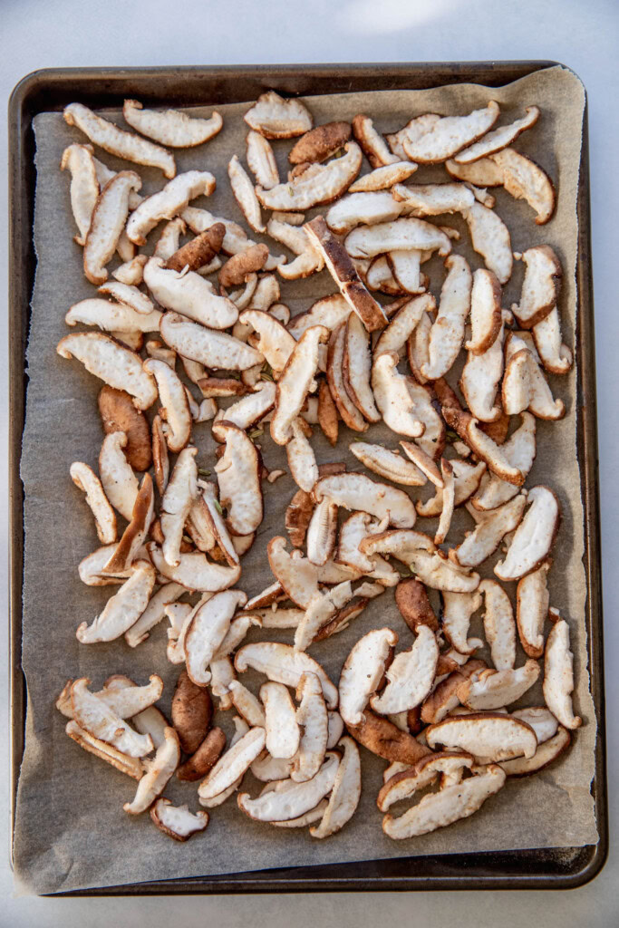 Seasoned thinly sliced mushrooms on a baking tray.