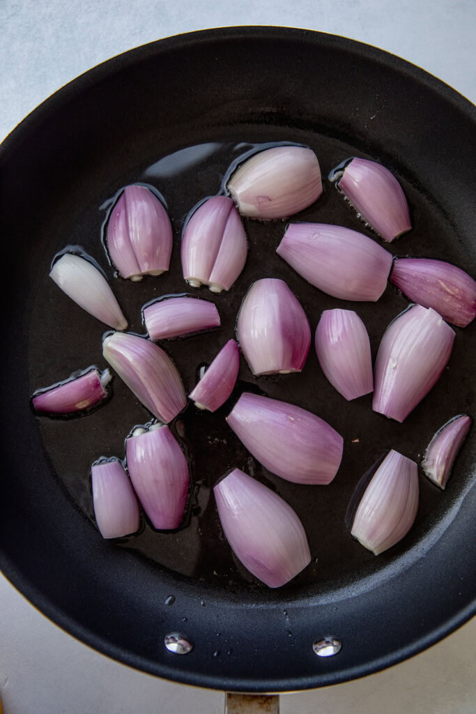 Halved shallots cut side down in a heated pan.