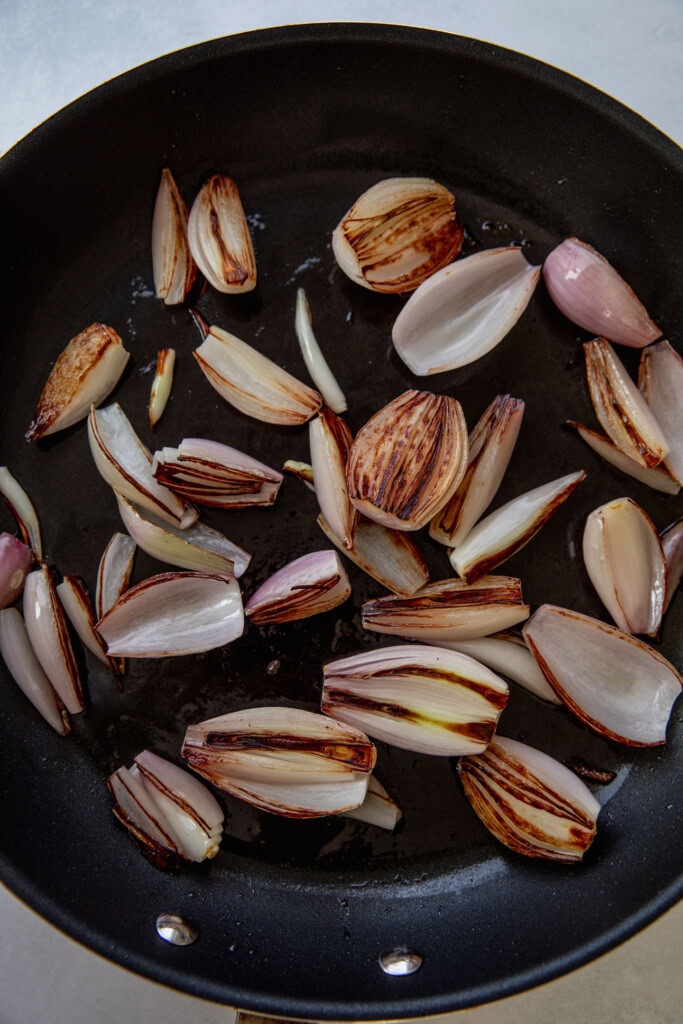 Charred shallots after flipping in a pan.