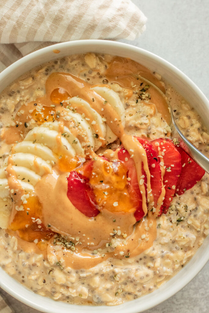 Close up of a bowl of pbj overnight oats topped with peanut butter, jelly, strawberries and banana slices in a bowl.