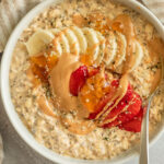 Bowl of ready to eat pbj overnight oats topped with peanut butter, banana, strawberries and extra jam.