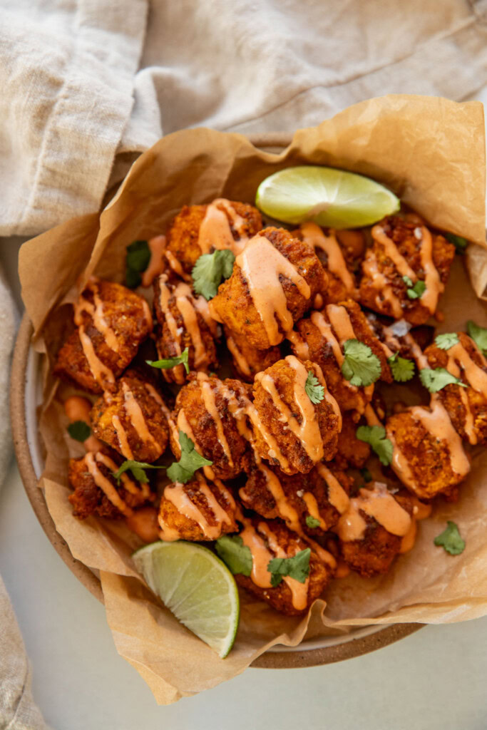 Parchment lined plate filled with the baked spiced tofu and drizzled with mayo ketchup and served with 2 lime wedges.
