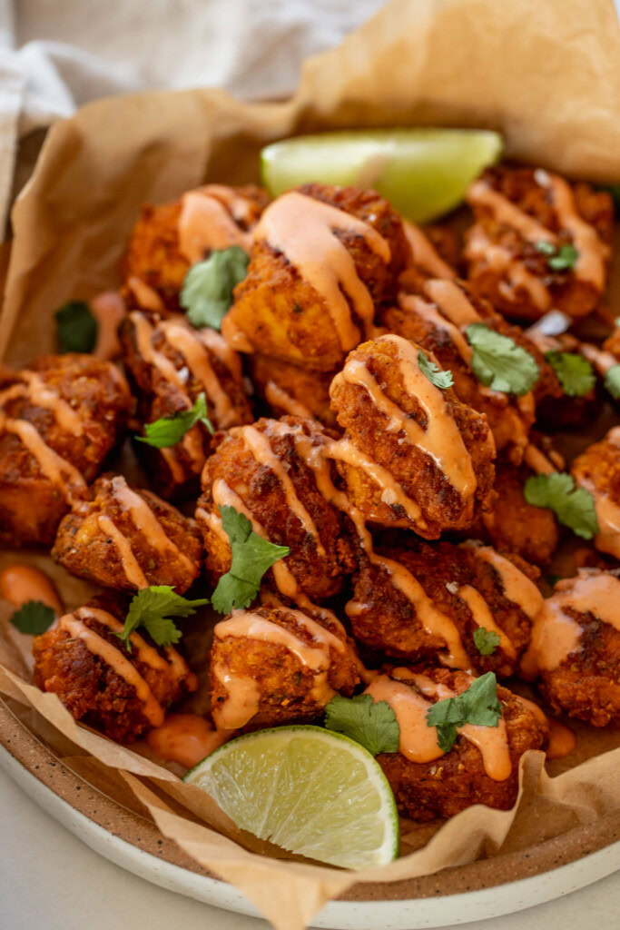 Close up of the pica tofu nuggets on a parchment lined plate served with lime wedges.