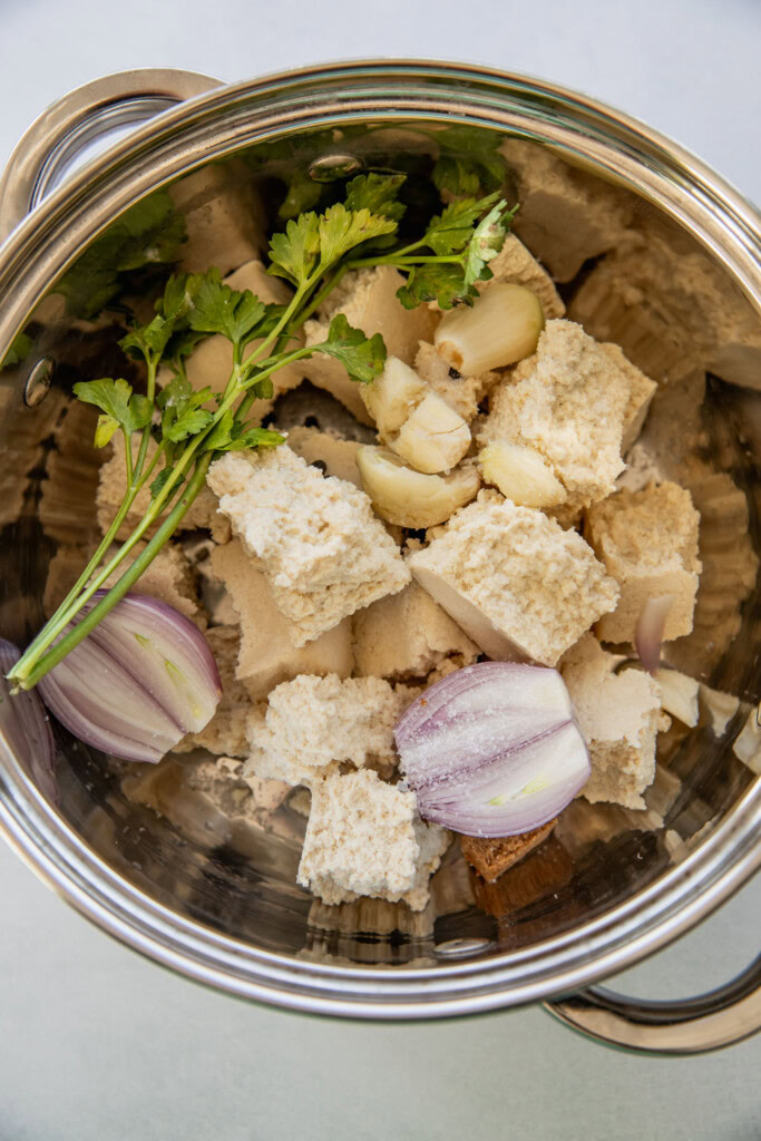 Pot filled with chunks of tofu, shallot, garlic, tamari, and cilantro sprigs.