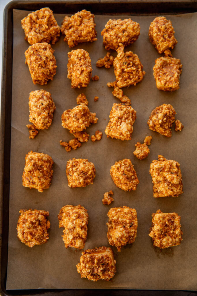 Seasoned tofu spread out on a parchment lined baking tray.