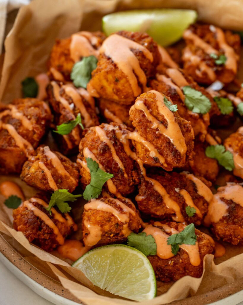 Close up of a plate of pica tofu on top of parchment paper and covered in a drizzle of mayo ketchup. Served with lime wedges.