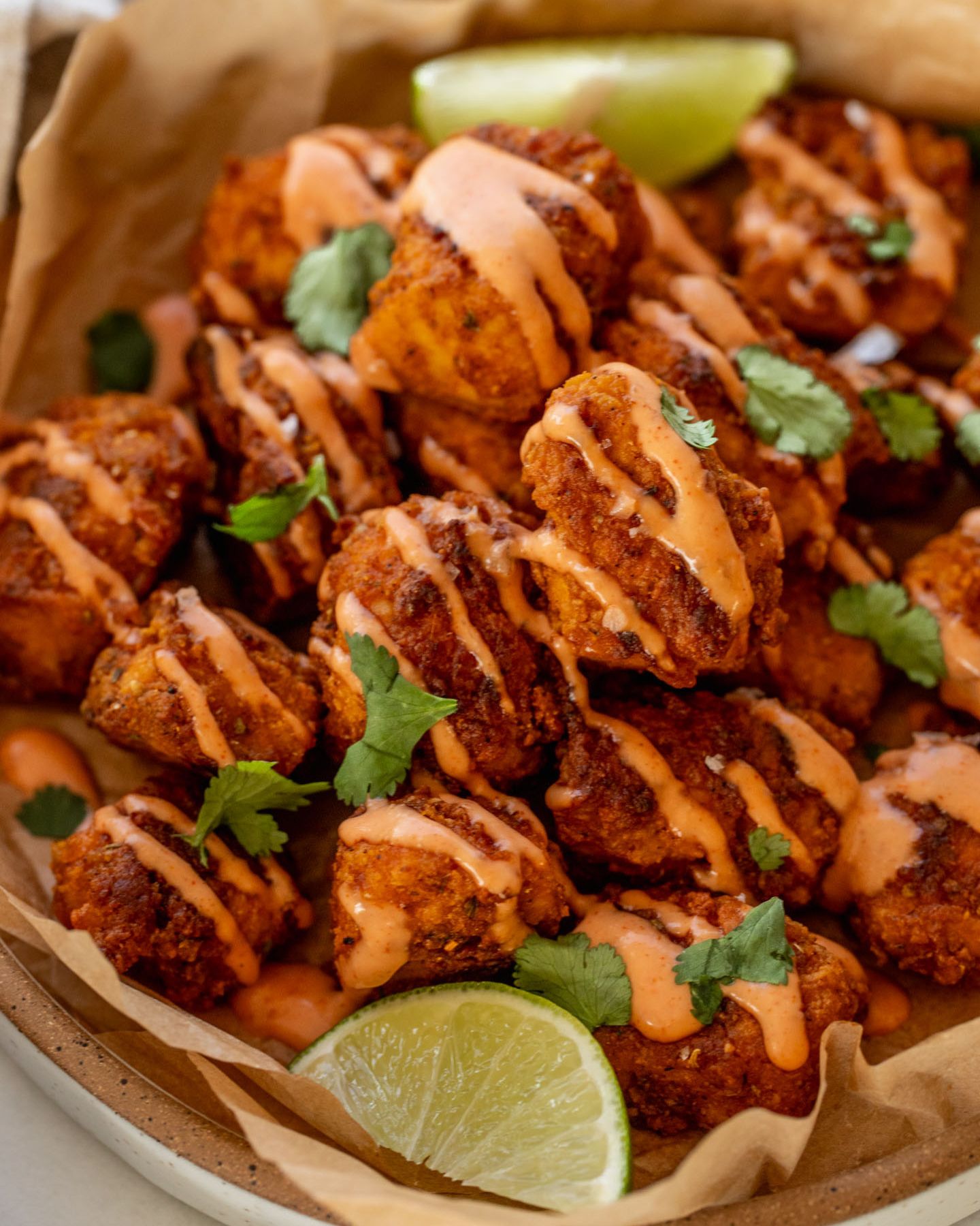 Close up of a plate of pica tofu on top of parchment paper and covered in a drizzle of mayo ketchup. Served with lime wedges.