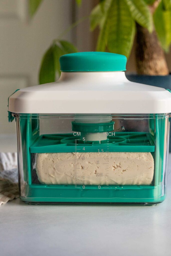 A commercial tofu press with spring to press the tofu block.