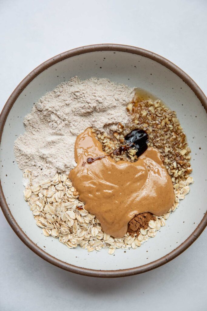 Mixing bowl with protein powder, oats, pecans, peanut butter, vanilla paste and cinnamon.
