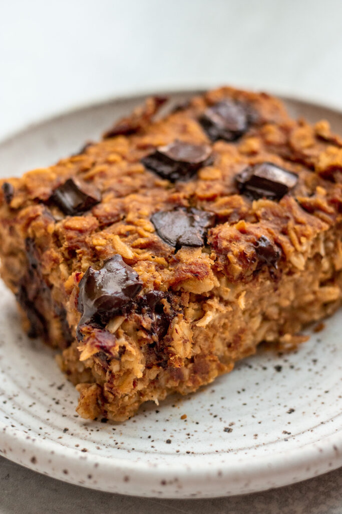 Side view of a slice of pumpkin baked oats on a white plate loaded with chocolate chips.