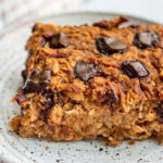 Close up shot of a slice of pumpkin baked oats on a plate loaded with chocolate chips.