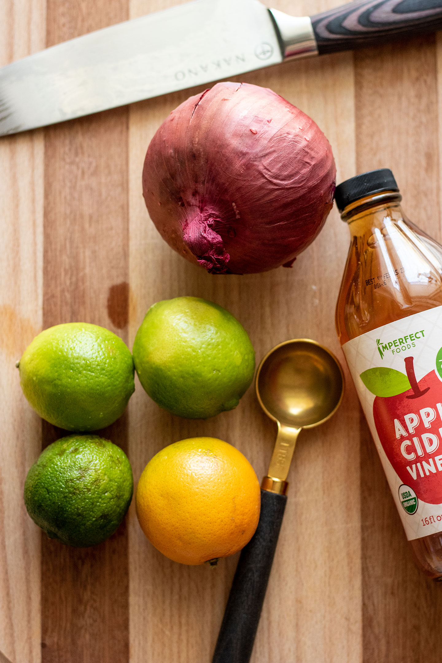 Limes, orange, onion and apple cider vinegar on a cutting board ready to be prepped.