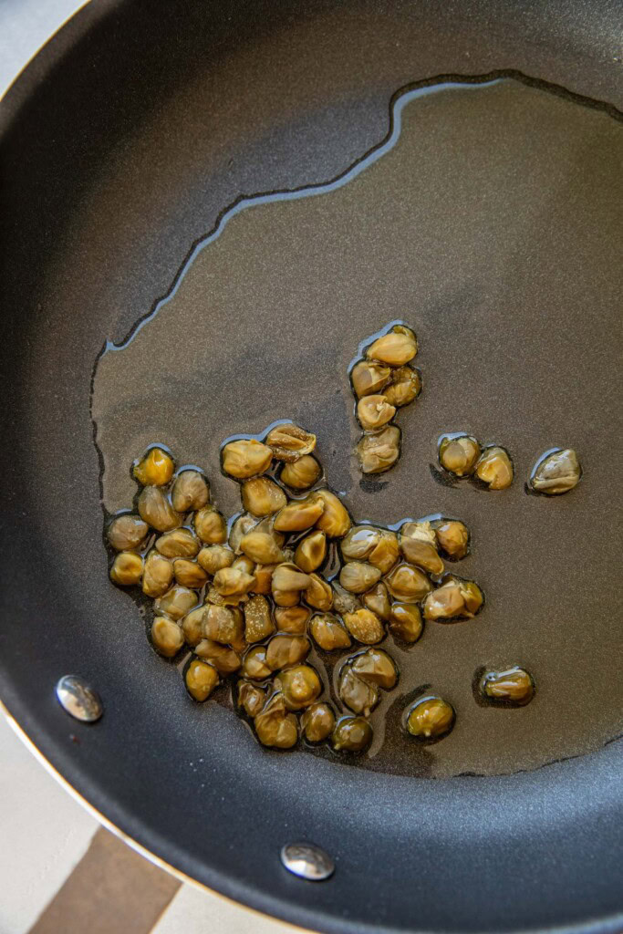 Capers cooking in a pan with oil.