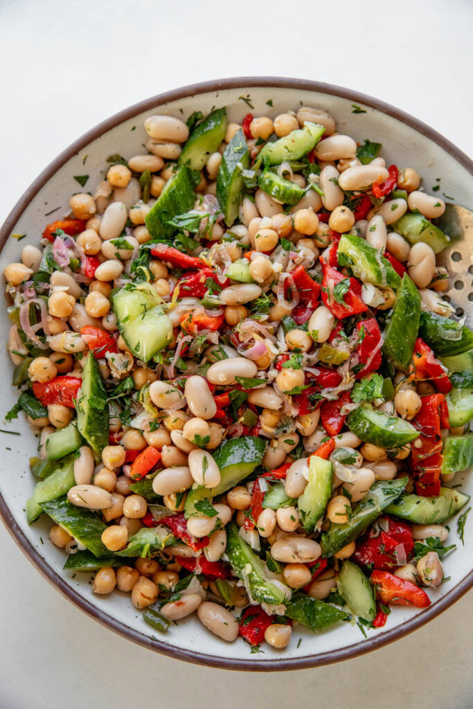 The beans, smashed cucumbers, roasted bell peppers, and shallot dressing mixed together in a bowl.