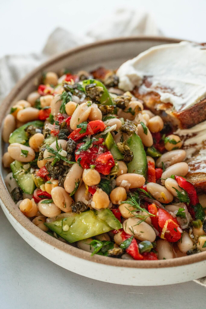 Serving the roasted bell pepper bean salad topped with fried capers and served with toasted bread smeared with cream cheese.