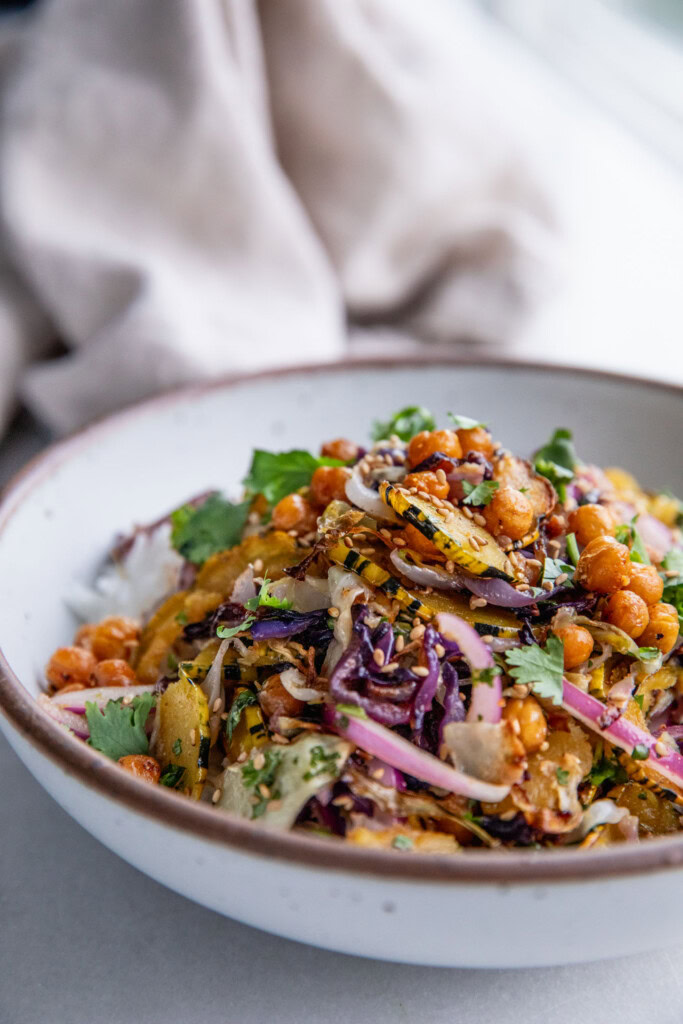 Side view of a bowl of rice topped wtih mixed roasted cabbage, squash, chickpeas and marinated onions.