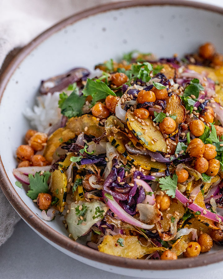 Close up of a bowl of rice topped with mixed roasted cabbage, squash, chickpeas and marinated onions.