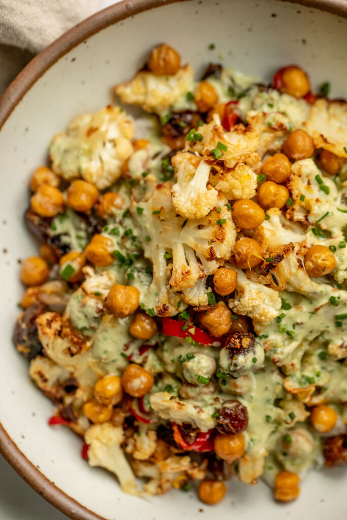 Close up of a bowl of rice topped with roasted cauliflower, dates and chickpeas and served with an herby tahini sauce.