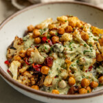 Side view of a bowl of rice topped with a cauliflower, date and chickpea salad and a creamy tahini dressing.