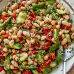 Giant bowl of mixed red bell pepper bean salad mixed together with a giant silver spoon.