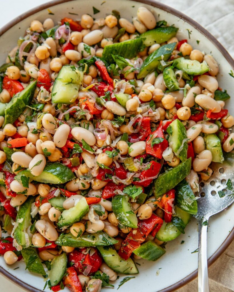 Giant bowl of mixed red bell pepper bean salad mixed together with a giant silver spoon.