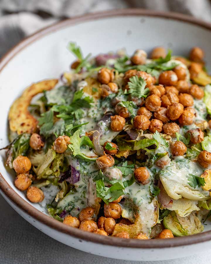 Side view of crispy roasted brussels sprouts and squash topped with crispy chickpeas and herby dressing.