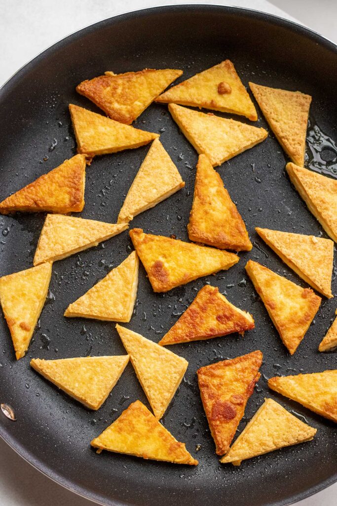 Searing tofu triangles in a large skillet.