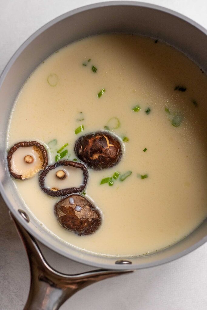 Sauce pan filled with soy milk, soy sauce, dried shiitake mushrooms and scallions.