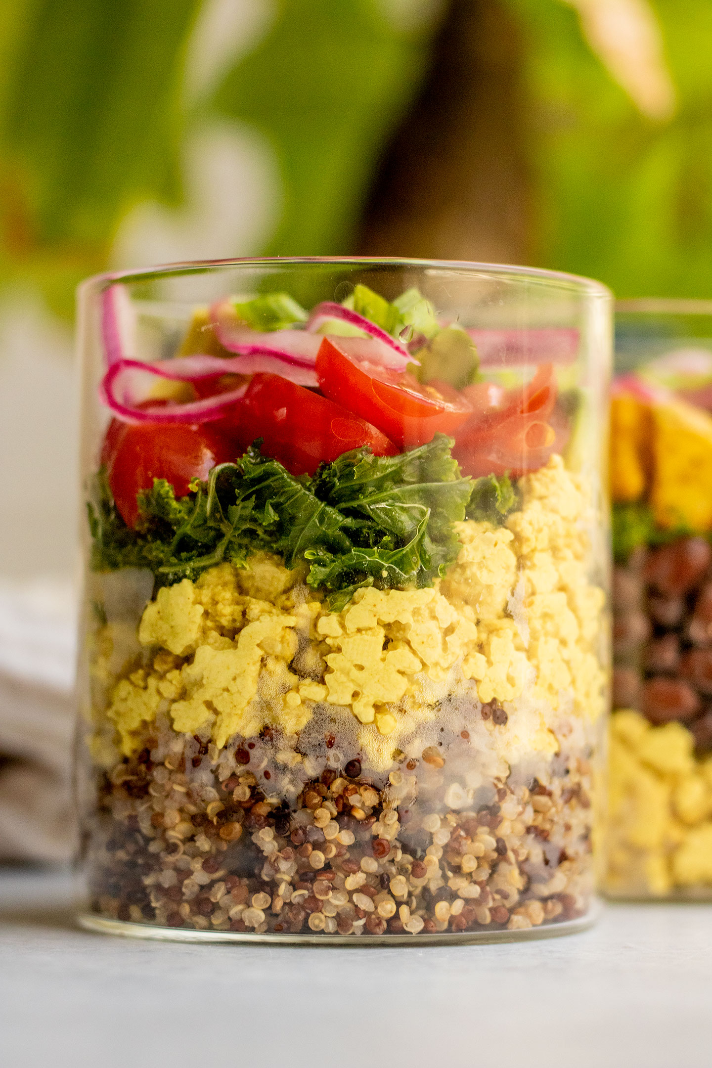 Close up of the jar filled with quinoa, tofu scramble, massaged kale, cherry tomatoes, and pickled onions.